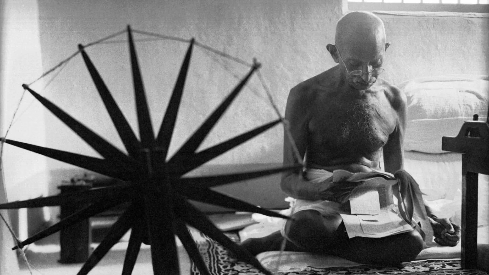 Mahatma Gandhi leyendo junto a una rueca portátil, instrumento utilizado por Gandhi para hilar hilo y hacer su propia ropa mientras estaba detenido como preso político en la cárcel de Yerwada.