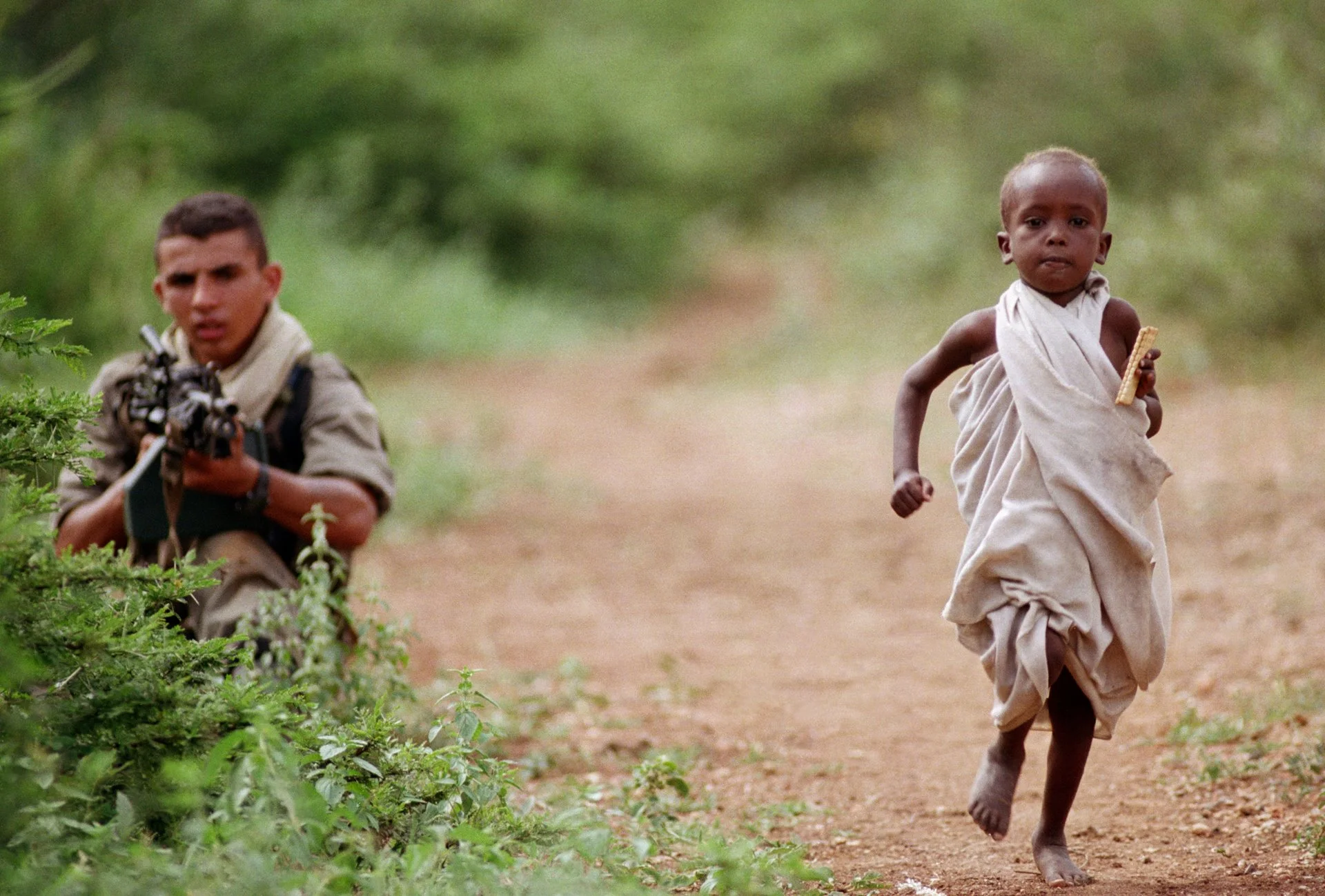Un niño somalí corre hacia un convoy de ayuda  en un pueblo a 25 km de Baidoa, el epicentro de la hambruna en Somalia. Un legionario francés vela por la llegada segura de los suministros.