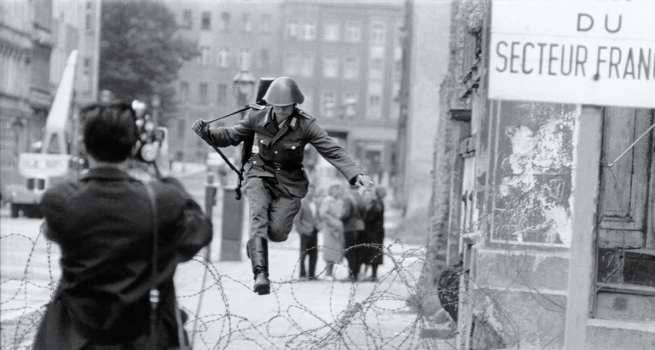 Era la época de la Guerra Fría. Berlín se dividió en dos: Berlín Este y Berlín Oeste. Al principio, el Muro de Berlín era una simple cerca de alambre de púas. En esta fotografía, un joven escapa hacia Berlín del Este.