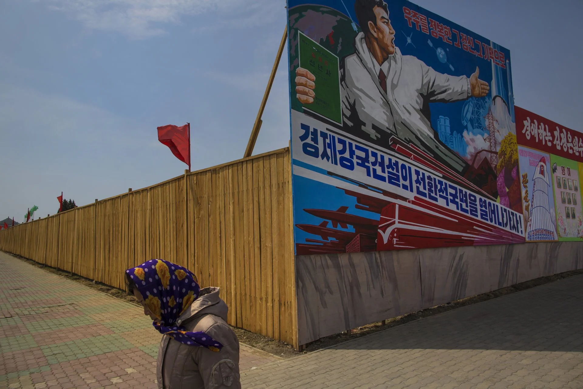 Una mujer pasa junto a vallas publicitarias en obras de construcción y un cartel de propaganda que muestra el lanzamiento de cohetes norcoreanos. 