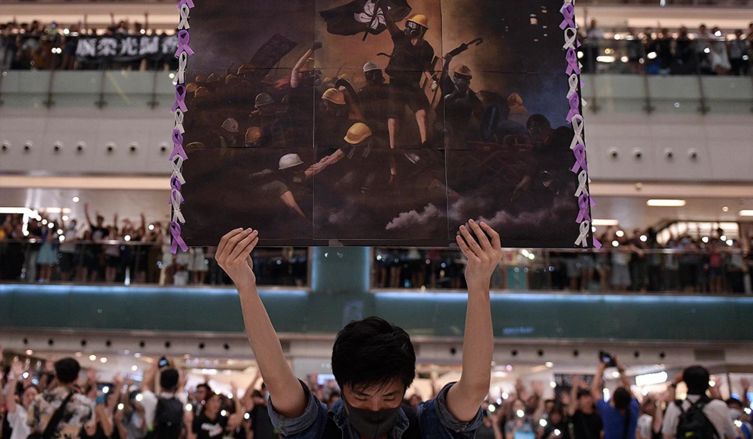 Um homem segura uma placa em Shatin, Hong Kong, enquanto as pessoas se reúnem para cantar "Glória a Hong Kong", uma canção de protesto que ganhou popularidade na cidade como um hino não oficial.