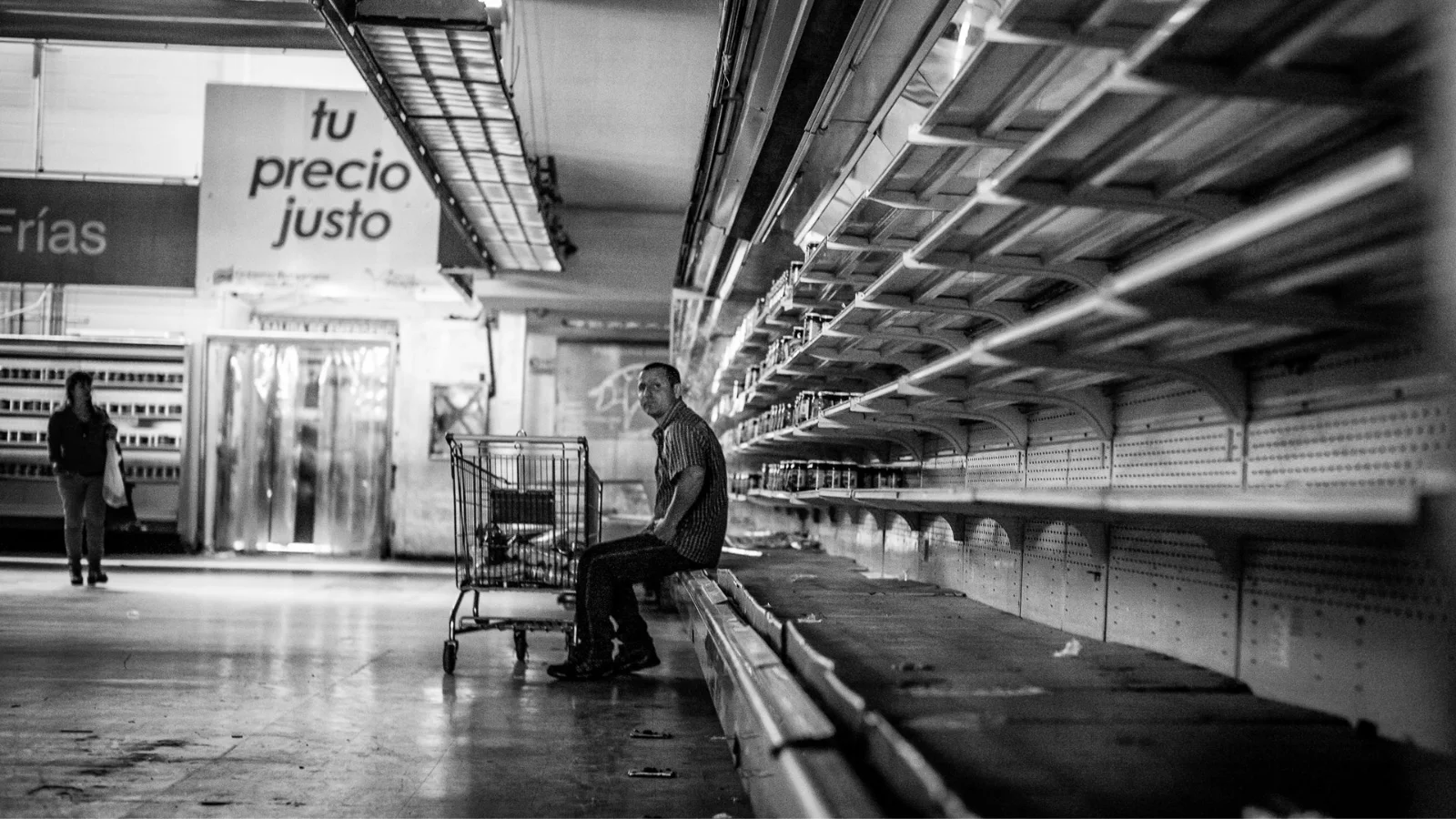 Um homem sentado em uma prateleira vazia de um supermercado estatal.