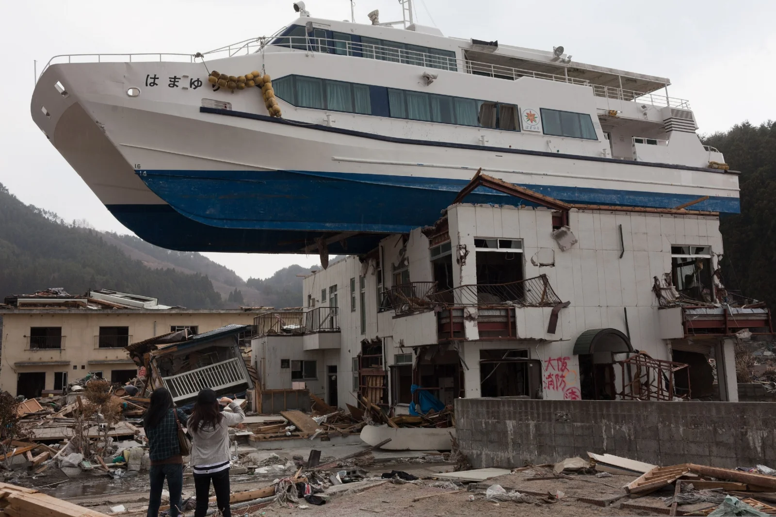 Nozomi Sabanai (izquierda) y su hermana miran un catamarán turístico arrojado por el tsunami sobre un edificio de dos pisos. Un sismo de magnitud 9.0 provocó el tsunami.