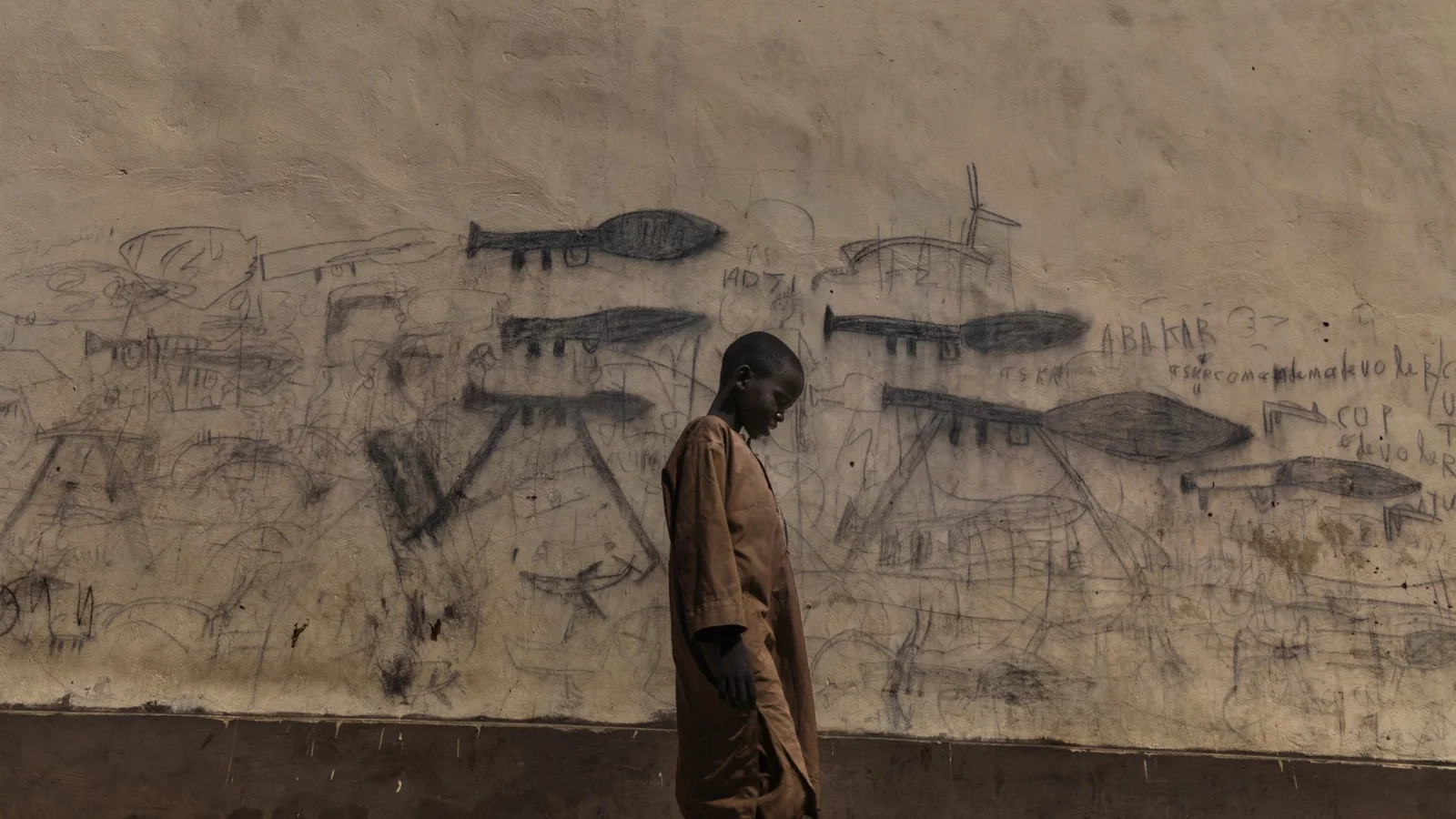 Мальчик-сирота проходит мимо стены с рисунками, изображающими реактивные гранатометы.