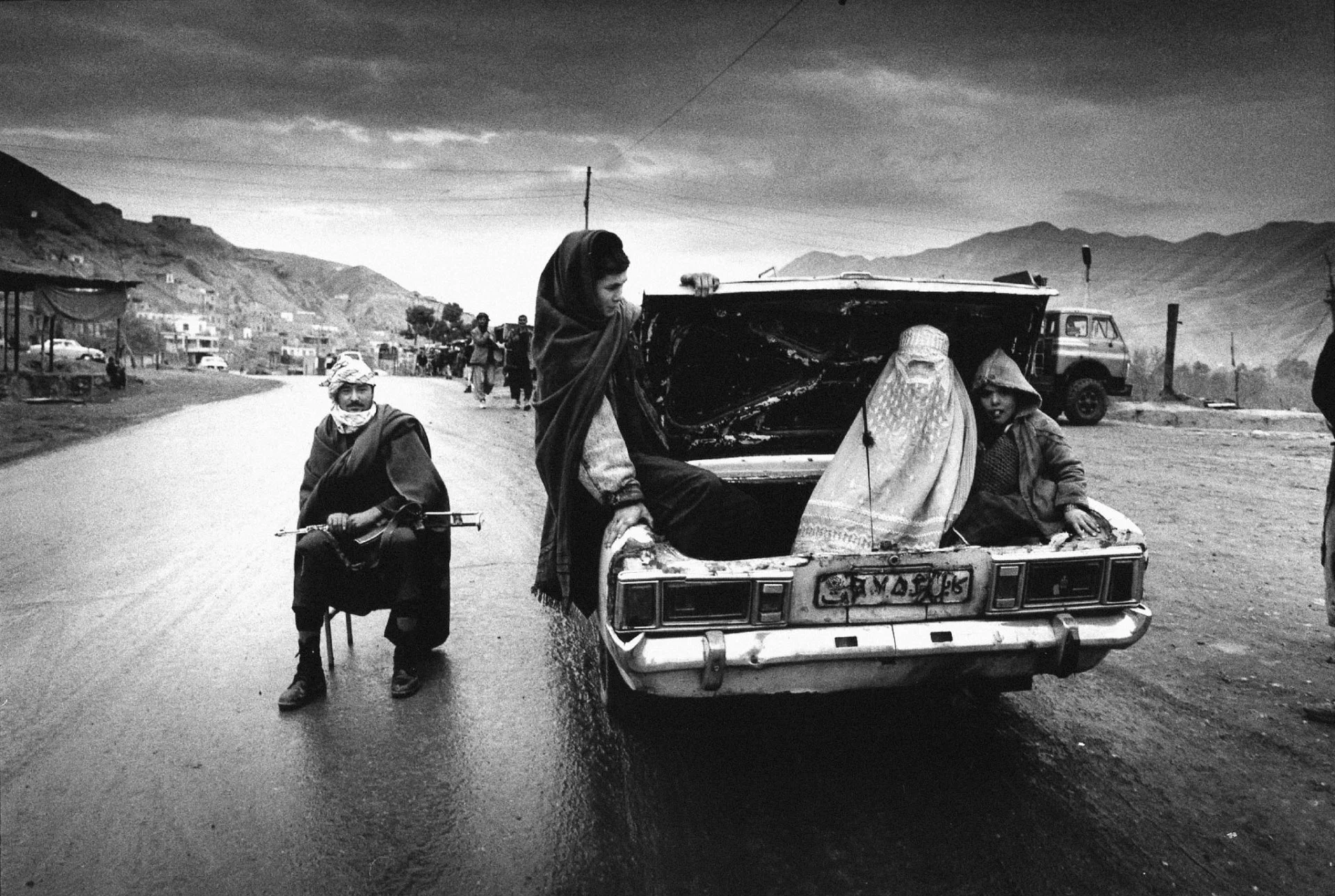 Un hombre armado custodia un puesto de control. Las mujeres no estaban permitidas sentarse con hombres dentro del automóvil. Después de años tragedias, los afganos intentan mantener sus tradiciones.