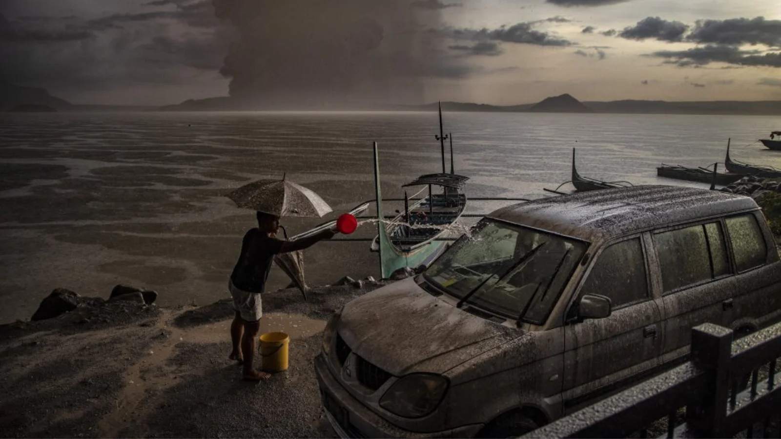 A resident of Talisay in Batangas washes a car, which is covered in volcanic ash mixed with rain, as the Taal volcano erupts.