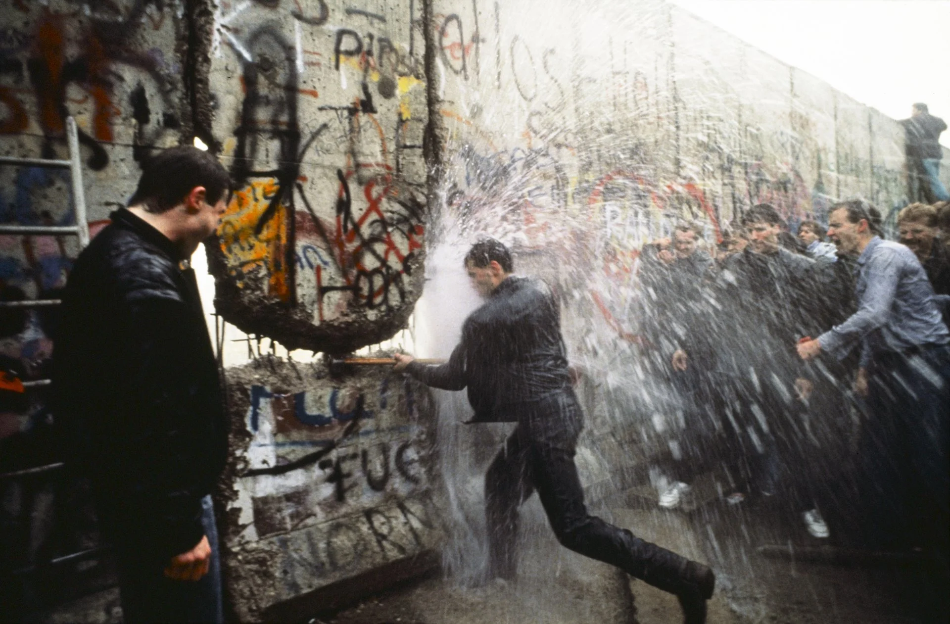 Después de martillar el muro cerca de la Puerta de Brandenburgo durante la noche, alemanes occidentales intentan escalar el Muro de Berlín, pero la policía los rechaza con un cañón de agua.