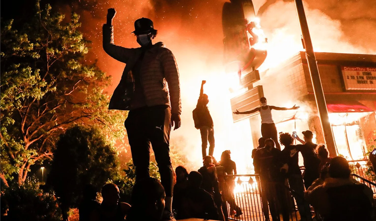 Los manifestantes levantan los puños en desafío frente a un restaurante de comida rápida en llamas cerca de la comisaría de los oficiales que arrestaron a Floyd, en Minneapolis.