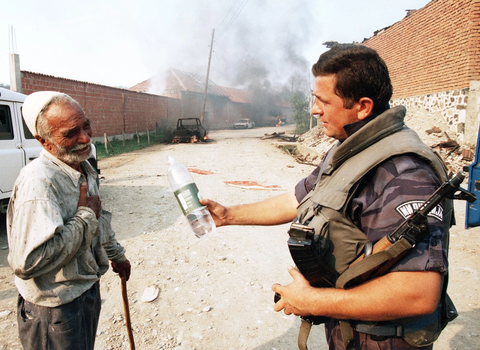 Un policía serbio ofrece agua a un anciano albanés en Kosovo. El anciano es el único residente que permaneció en Glodjane después de que la policía serbia retomara la aldea de manos del ELK.